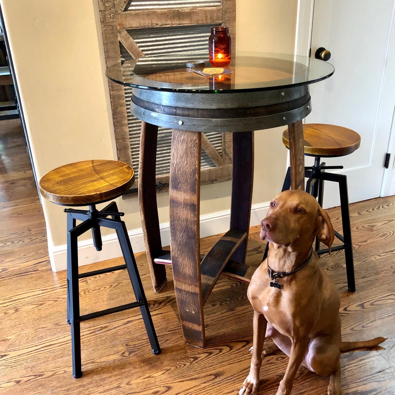 Dog sits near a barrel table with stools and a candle