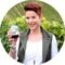 Woman with red hair smiles, holding a glass of red wine in vineyard